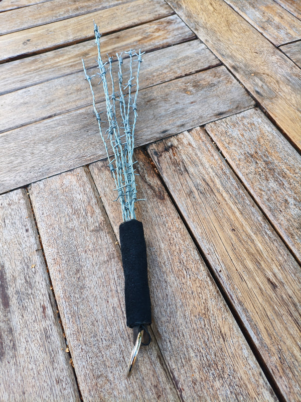 Martinet AdryX en fils barbelés, 54 cm, manche gainé noir et anneau, posé sur une table en bois