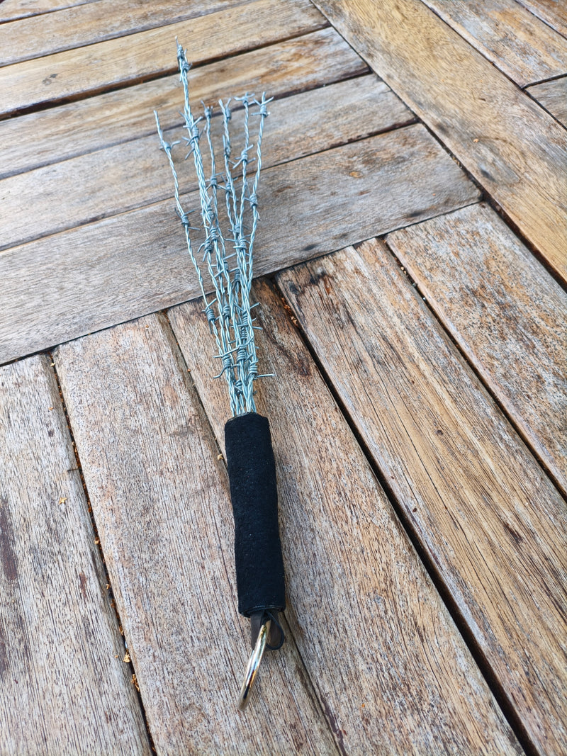 Martinet AdryX en fils barbelés, 54 cm, manche gainé noir et anneau, posé sur une table en bois