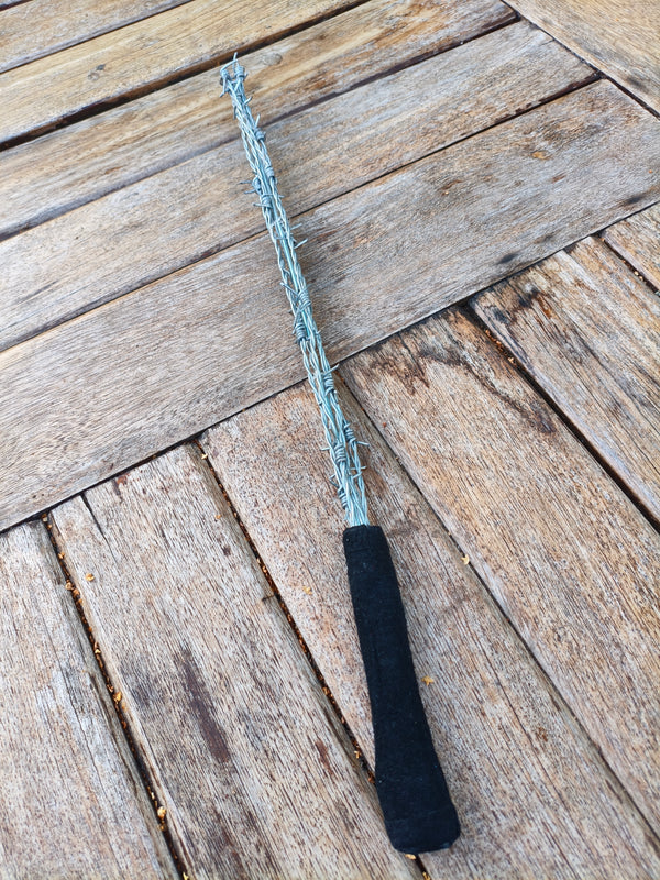 Badine AdryX en fils barbelés, 51 cm, poignée en cuir retourné noir, posée sur une table en bois