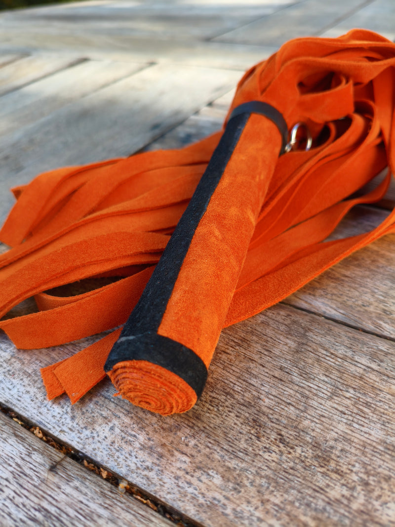 Détail de la poignée en cuir orange bordée de noir du martinet doux AdryX, fait main en France