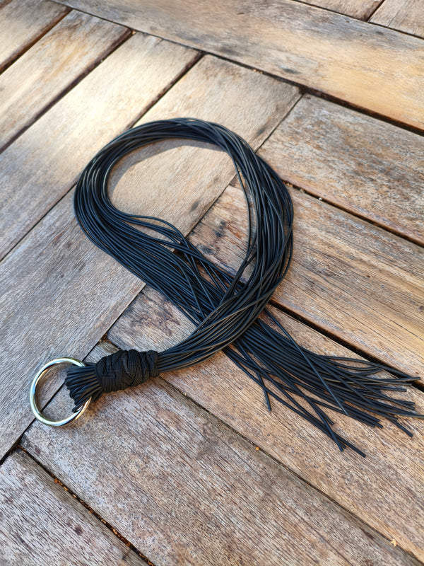 Martinet long AdryX en lanières de caoutchouc noir, 80 cm, posé en boucle sur une table en bois avec son anneau métallique