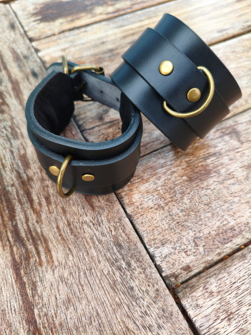 Les deux menottes en cuir noir AdryX fermées et posées l'une sur l'autre, doublure visible à l'intérieur