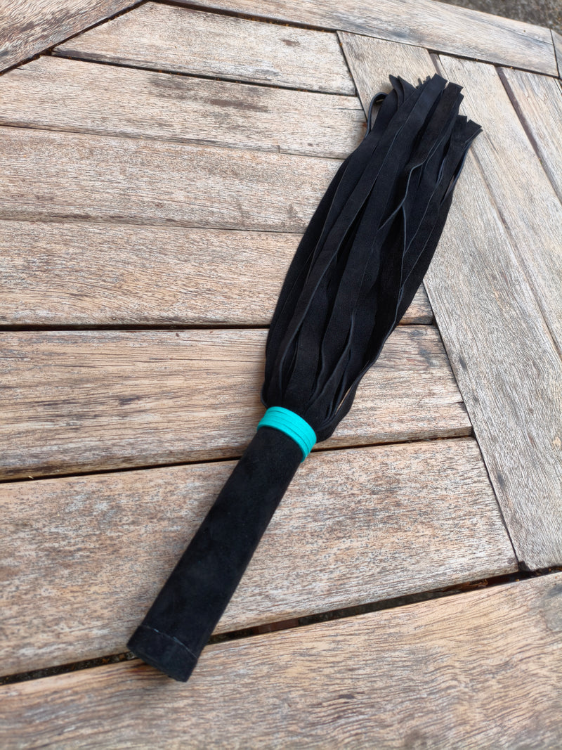 Martinet AdryX en cuir noir à bague turquoise, vue d'ensemble sur une terrasse en bois, lanières déployées