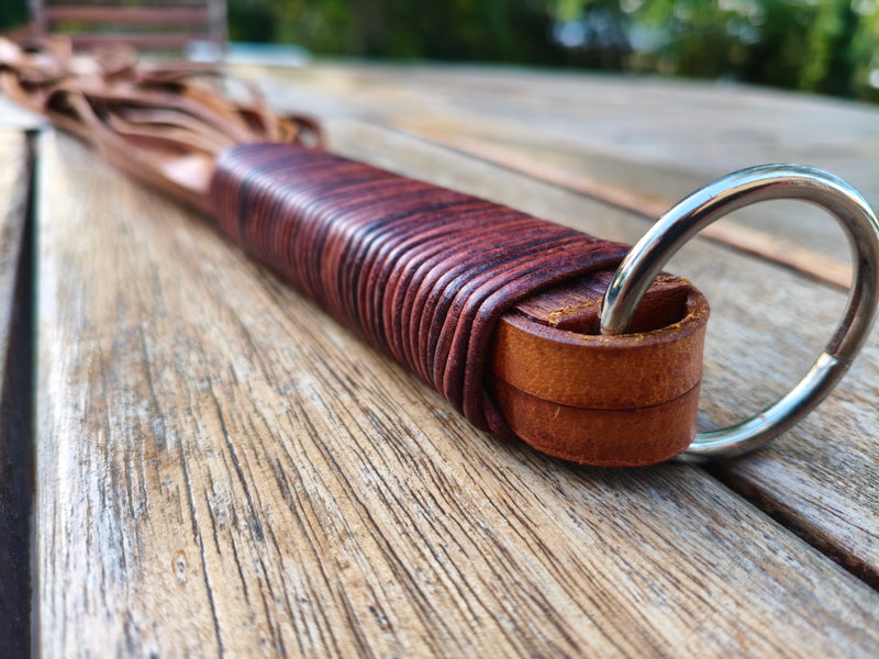 Détail du manche du flogger lourd AdryX : ligature en cuir brun et anneau de suspension en métal