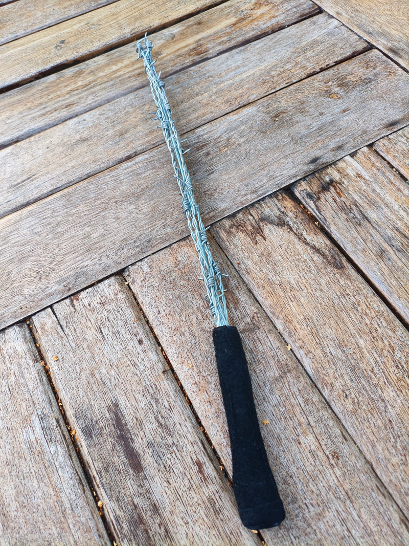 Badine AdryX en fils barbelés, 51 cm, poignée en cuir retourné noir, posée sur une table en bois