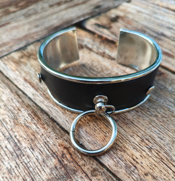 Bracelet manchette AdryX en cuir noir pleine fleur à monture argentée, anneau mobile, posé sur une table en bois