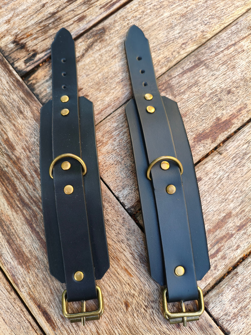 Les deux menottes en cuir noir AdryX à plat, anneaux en D et rivets en laiton